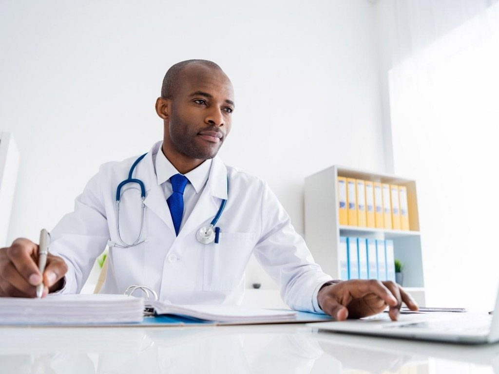 a male doctor sitting at a desk focused on a laptop