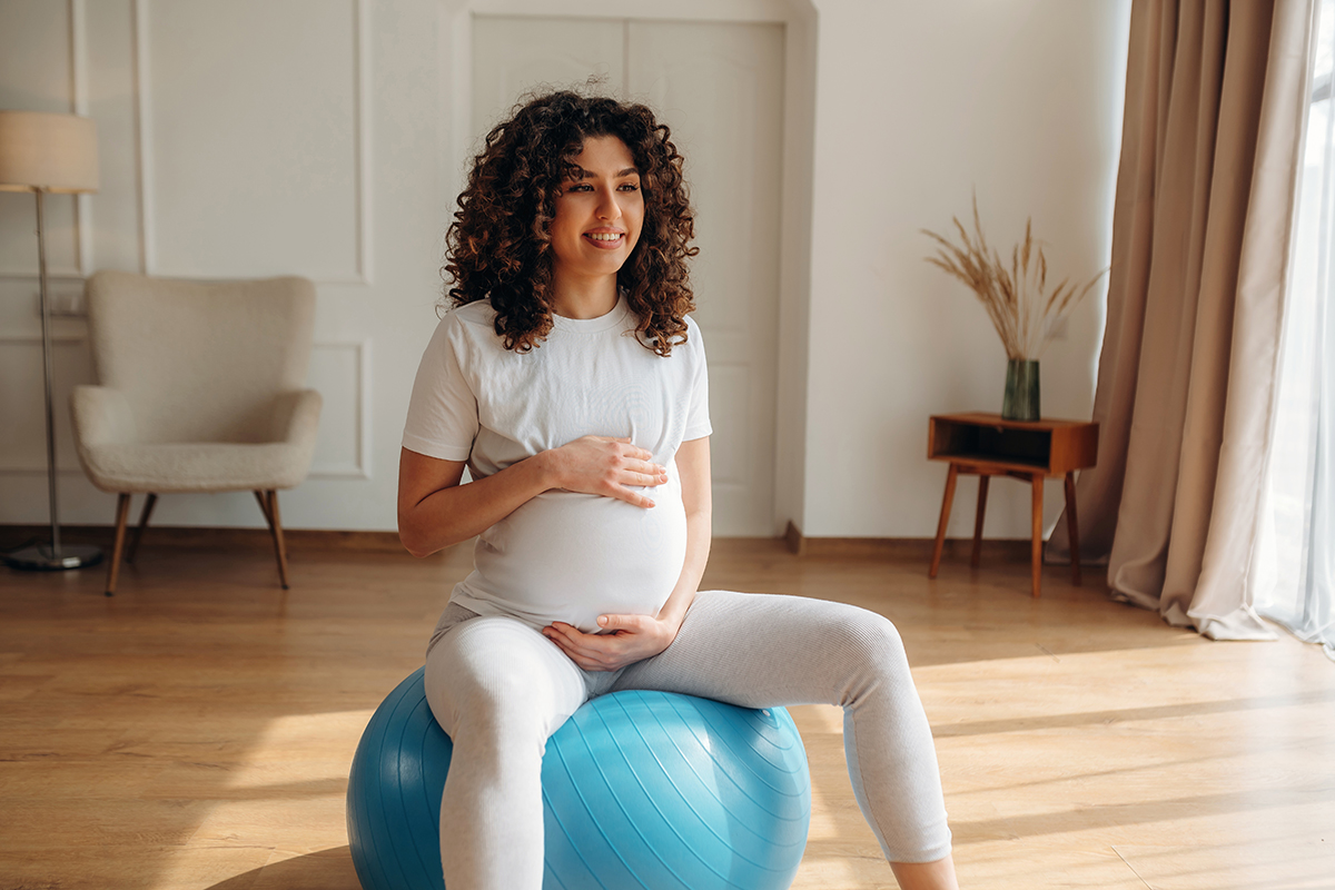 Pregnant person sitting on a stability ball during prenatal exercise.