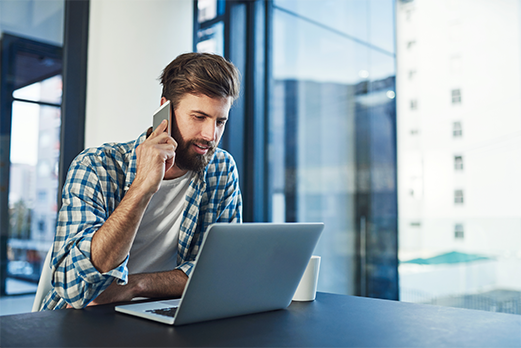 Man talking on smartphone looking at laptop computer