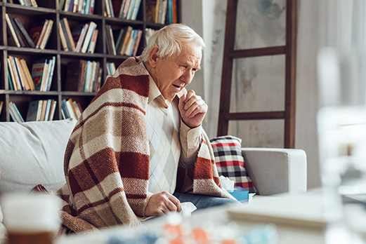 MVPDig0055_Flu Shots_Side Images_Everyday Prevention_202508 an older man sitting on a couch wrapped with a blanket and coughing