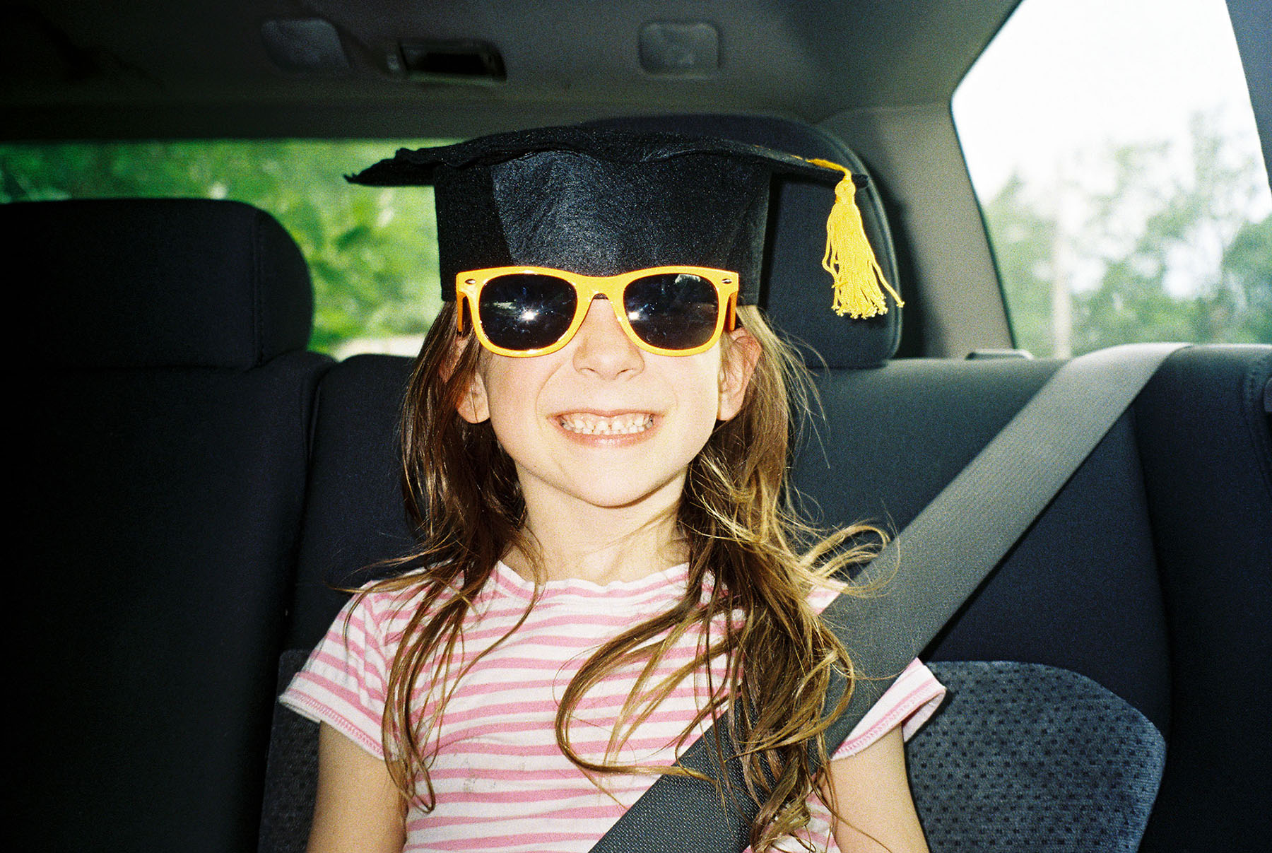 young girl wearing graduation cap and sunglasses in car