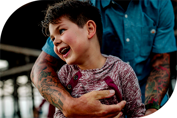 Niño sonriente con el brazo tatuado de un adulto a su alrededor.