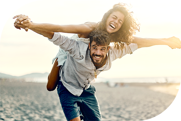 Couple enjoying time together at the beach, one person giving the other a piggyback ride