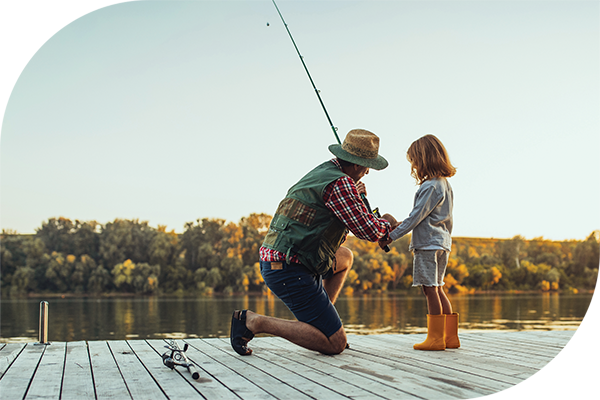 Adult kneeling to teach a child to fish. 