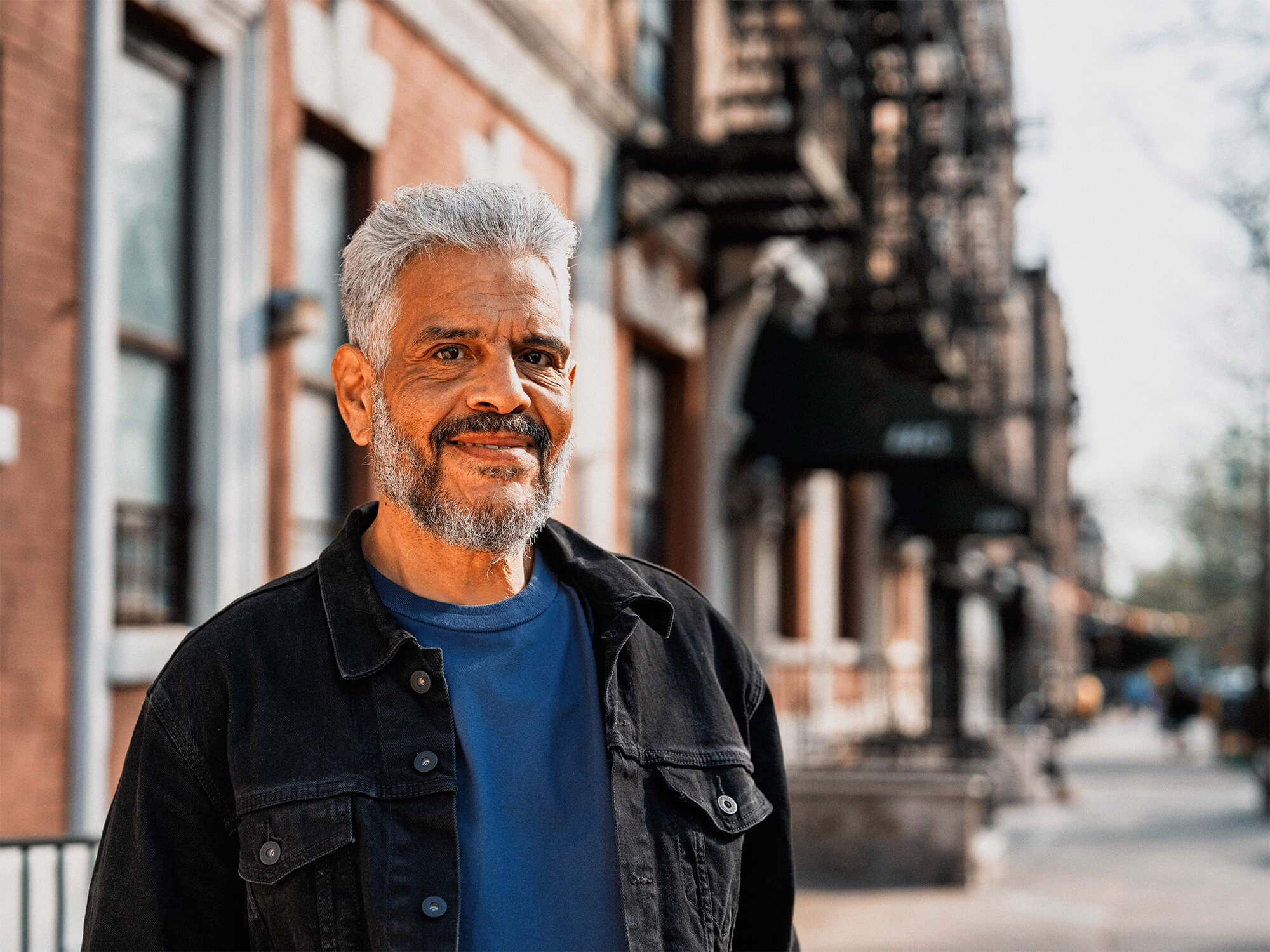 a man with grey hair and a beard stands on a city street