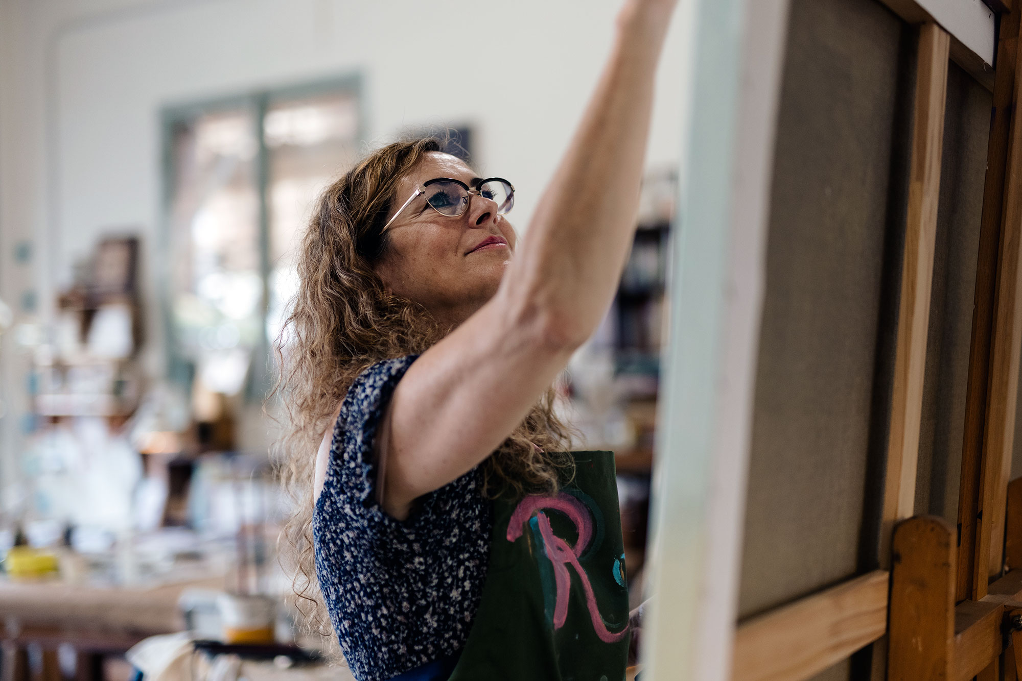 a woman painting a canvas in an art studio full of supplies