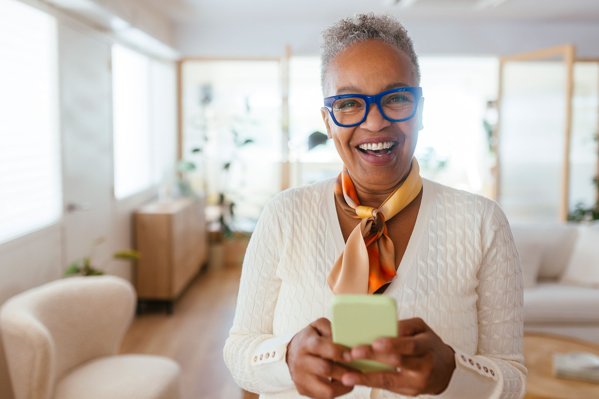 a woman with glasses and a scarf smiling while holding a green cell phone