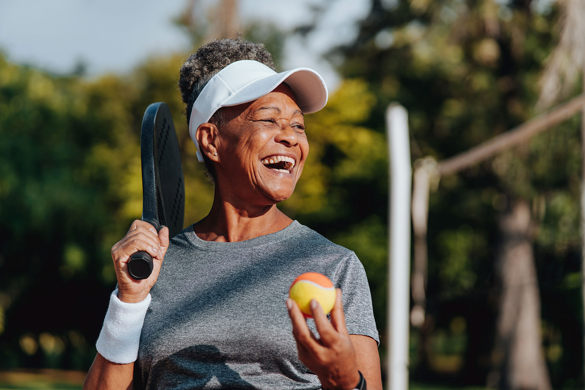 older woman outdoors holding a tennis ball and racket