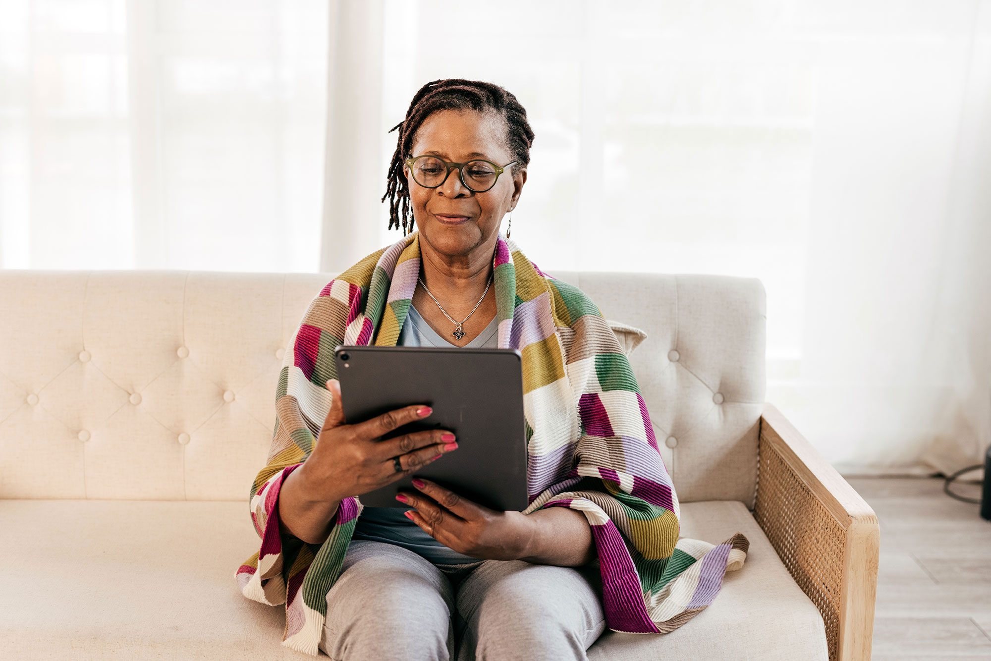 an older woman sits on a couch indoors holding a tablet