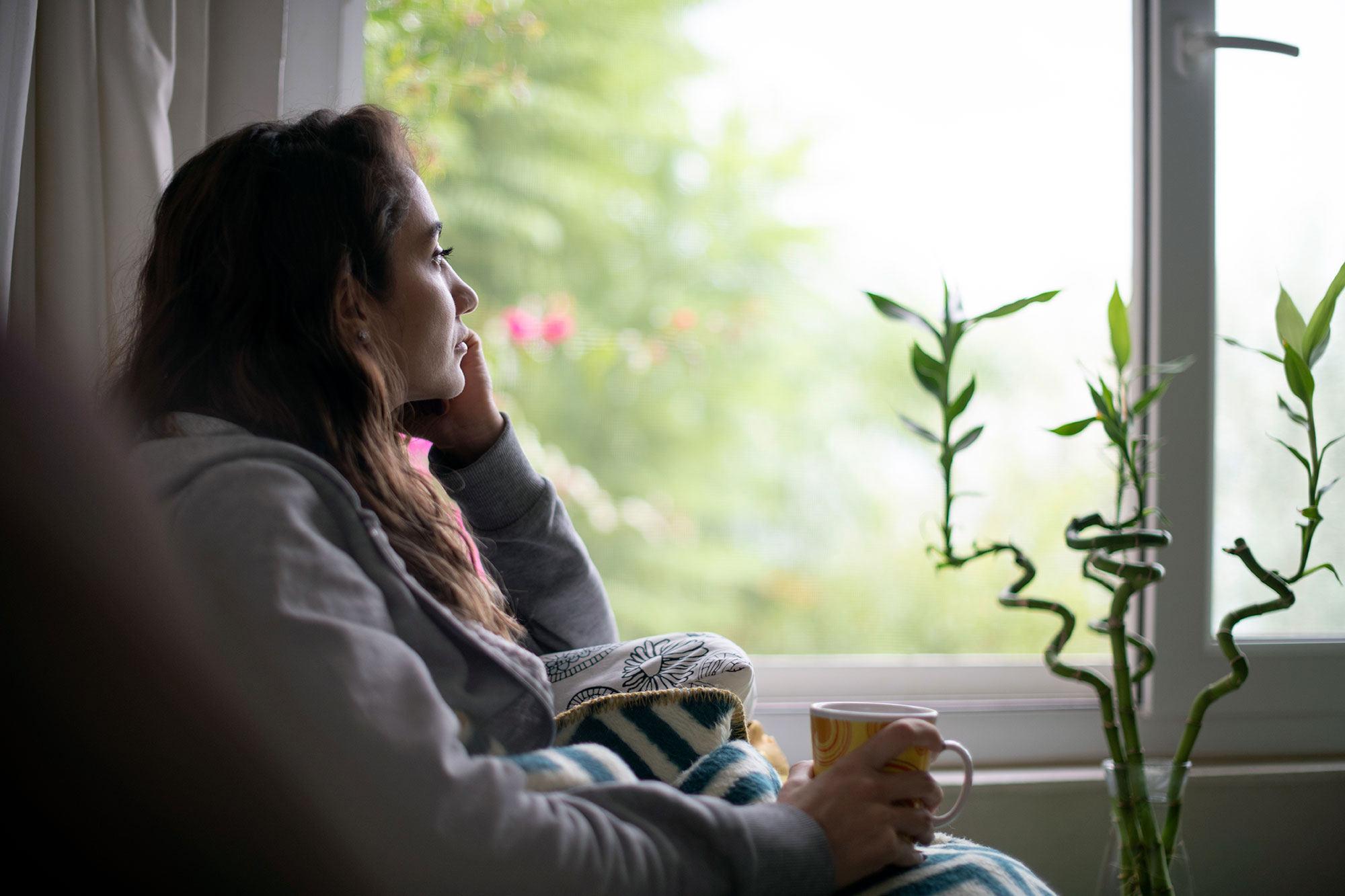 a woman relaxes indoors with a mug looking out the window