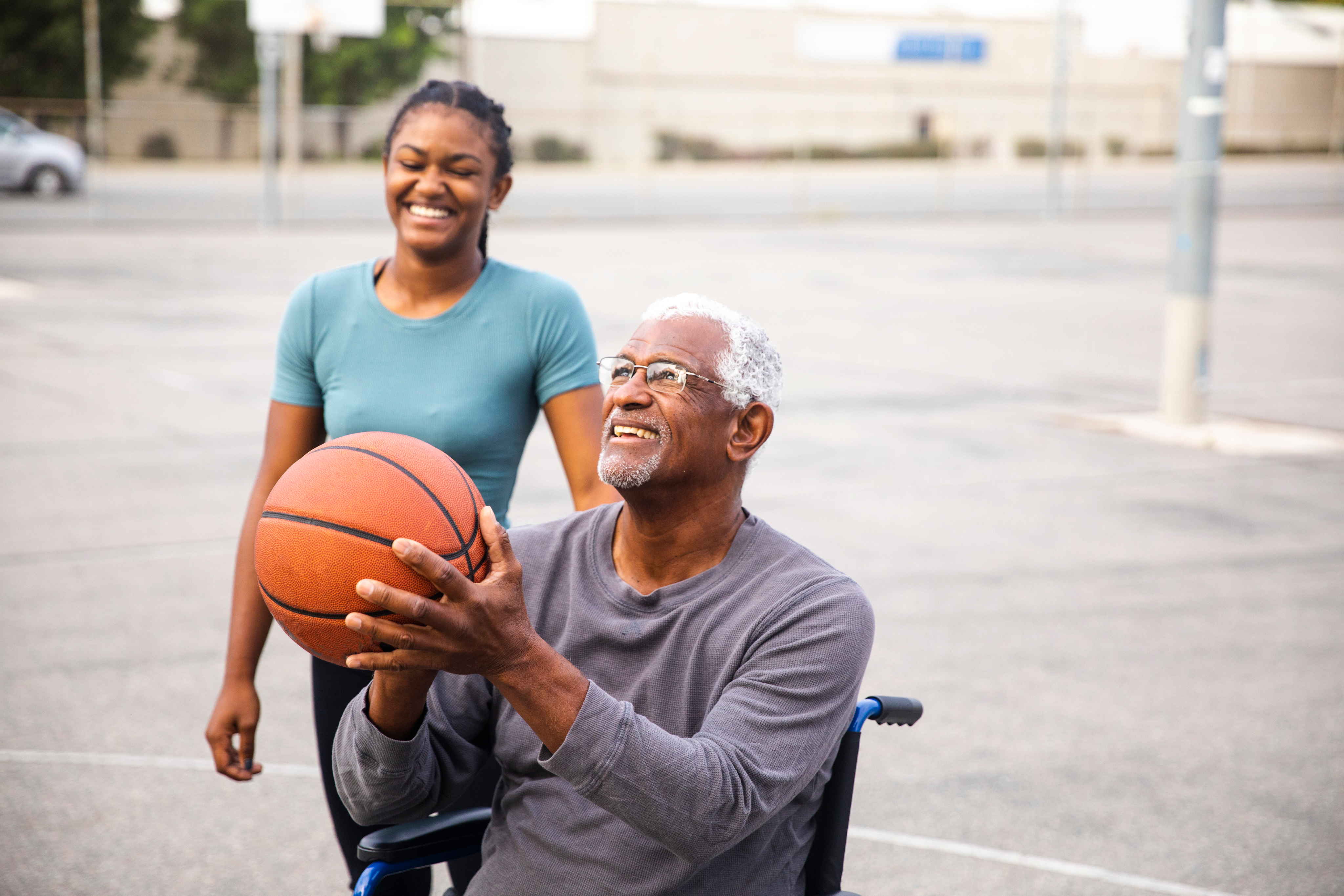 older adult wheelchair user shooting basketball with young person