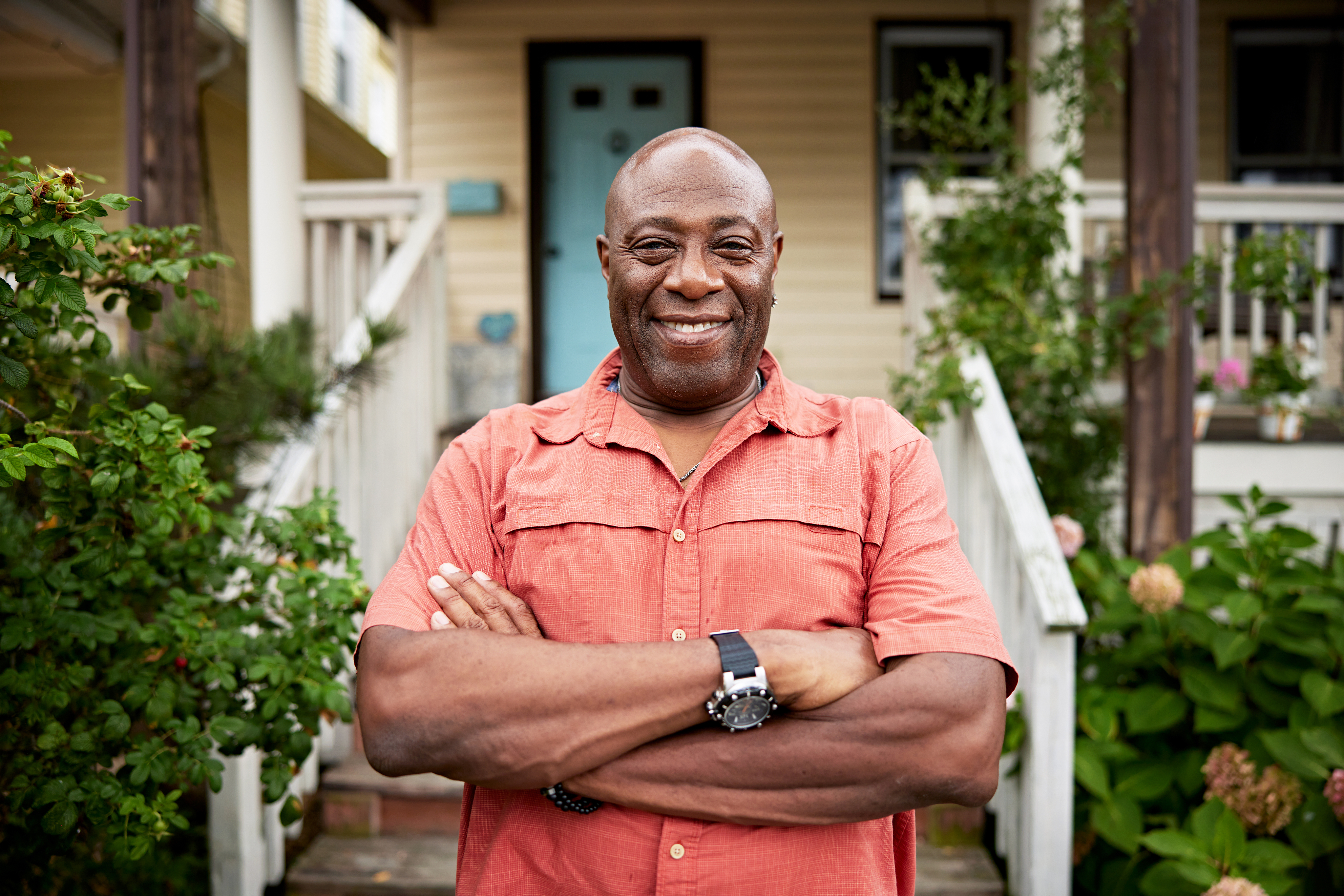 man with arms crossed smiling outside house