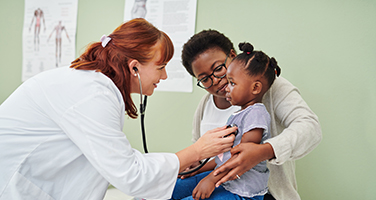 Doctor examining a young child while a caregiver holds the child