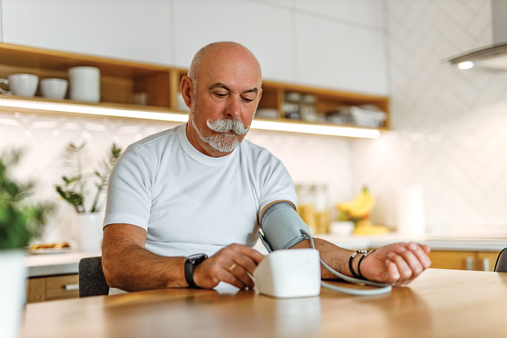 older man checking his blood pressure in his kitchen