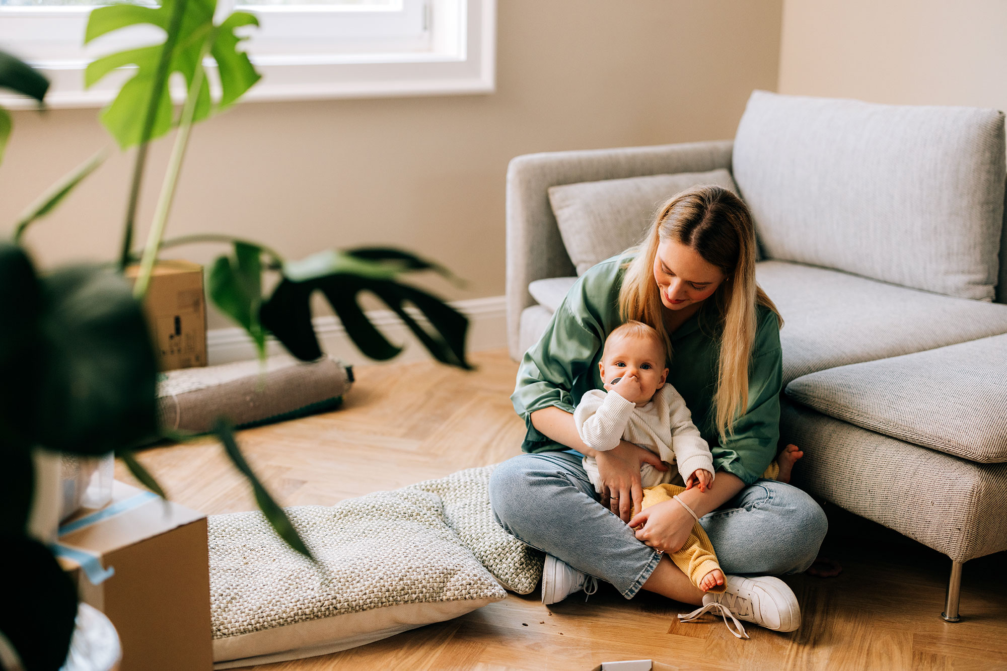 woman sits on floor in a living room holding a baby